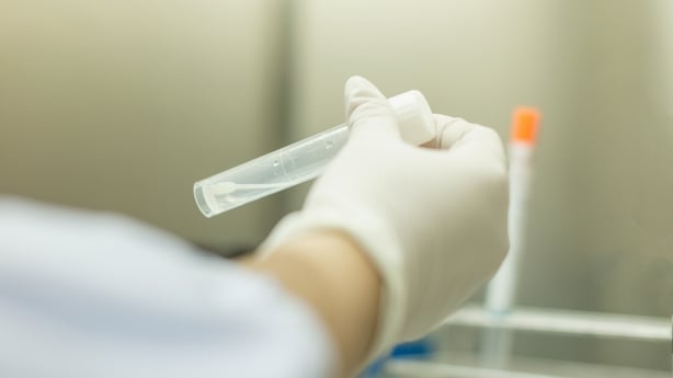 Closeup image of a doctor's hand wearing a white glove holding a test tube containing clear liquid.
