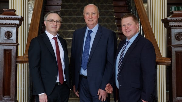An image of three business men pictured at the bottom of a big staircase