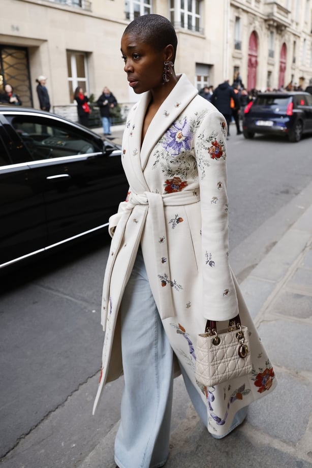 Rachel Jones wears white flower decorated coat, light wash wide leg jeans, cream Dior bag