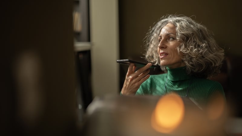 Mature business woman with gray hair is speaking to AI virtual assistant on her smartphone, planning meetings.