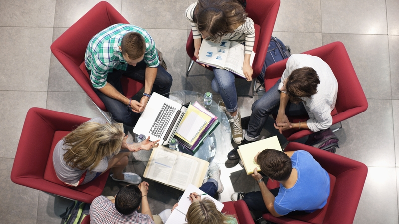 Top down picture of university students studying in a circle, sitting on red chairs and using laptops, books and notepads (Getty Images)