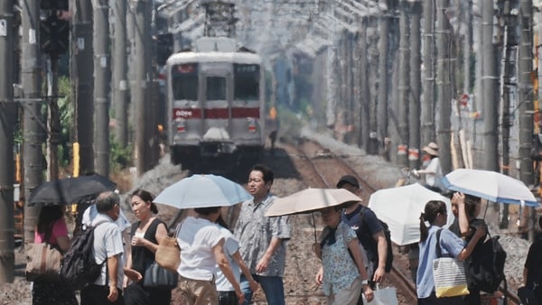 Heat haze is seen in the background while pedestrians with umbrellas cross a railroad on a hot day in Tokyo