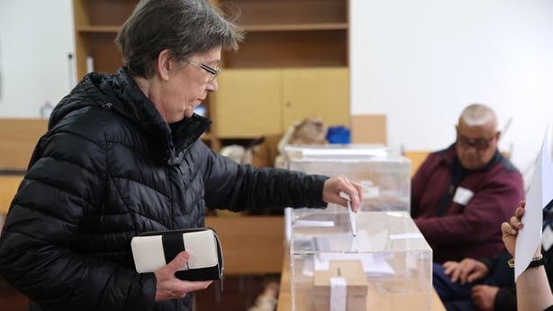 a woman casts her vote into a plastic ballot box