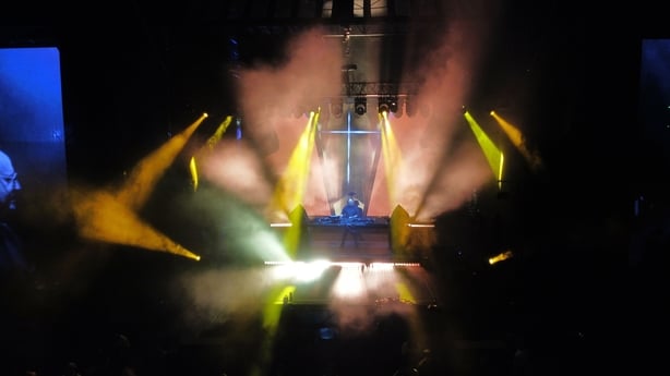 Strobe lighting flashes across a stage with a DJ at the centre