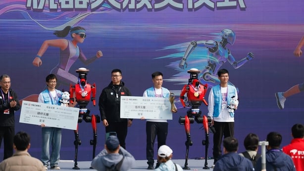 two humanoid robots are seen on a stage with four men