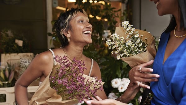 Happy young women with flower bouquets laughing at shop