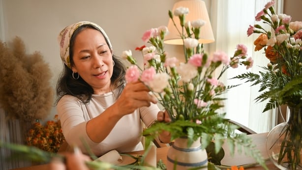 Pleasant Asian senior woman making a bouquet with fresh flowers at floral shop. 