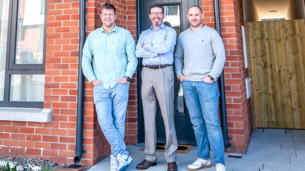 Three men pose outside a new house 