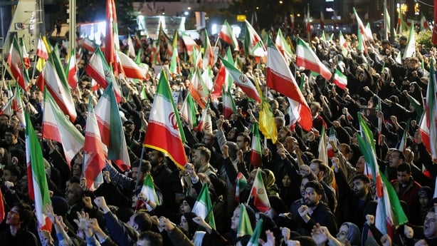 a huge crowd of people with many waving Iranian flags