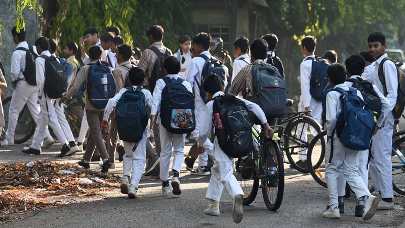 children wearing school uniforms carry backpacks and push bicycles