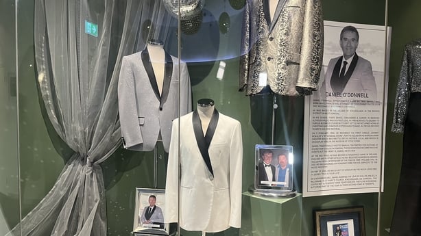 a number of suits are displayed in a glass case with a photograph of daniel o'donnell 