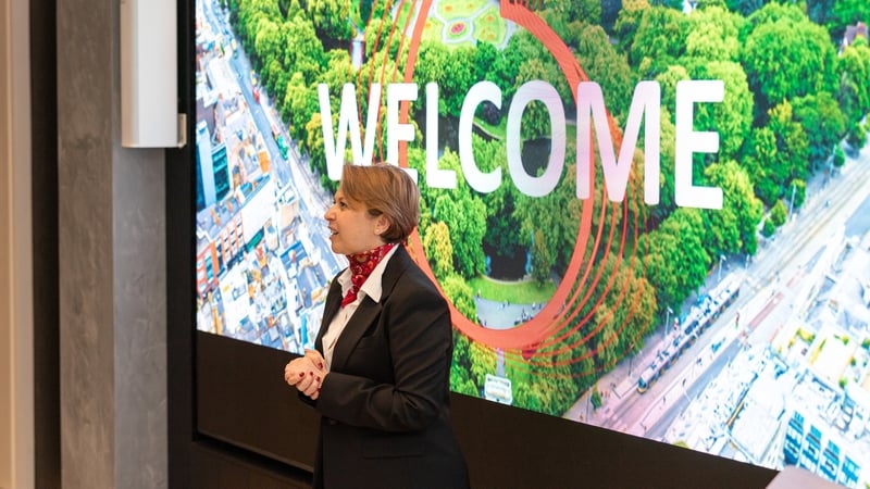 Image of a business woman talking on a stage with a city scape in the background