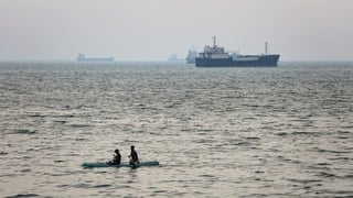 BANDAR ABBAS, IRAN - APRIL 22: Two boys paddle-board in the sea as ships are anchored near the shoreline on April 22, 2026 in Bandar Abbas, Iran. Bandar Abbas is a port city and the capital of Hormozgan Province, along the Persian Gulf and Strait of Hormu