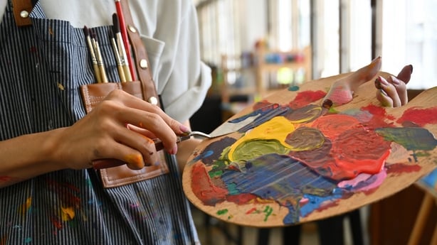 Close-up image of a young creative artist's hands smeared with watercolors holding a spatula mixing color on a palette.
