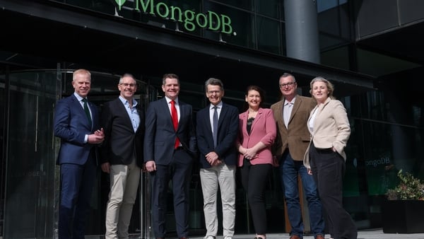 Seven people stand in a row outside an office building with a sign reading 'mongoDB'