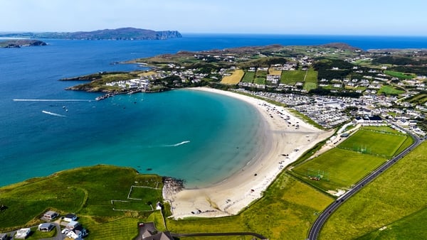 Stunning high-angle visual of the expansive, crescent-shaped coastline of Sheephaven Bay, highlighting both the popular Blue Flag Downings Beach and the dramatic dune-backed expanse of Tramore Beach, adjacent to the renowned Rosapenna Golf Resort. The sce