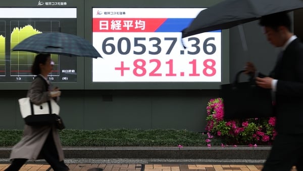 Closing figure of the Nikkei index displayed outside a securities firm in Tokyo as people walk by with umbrellas