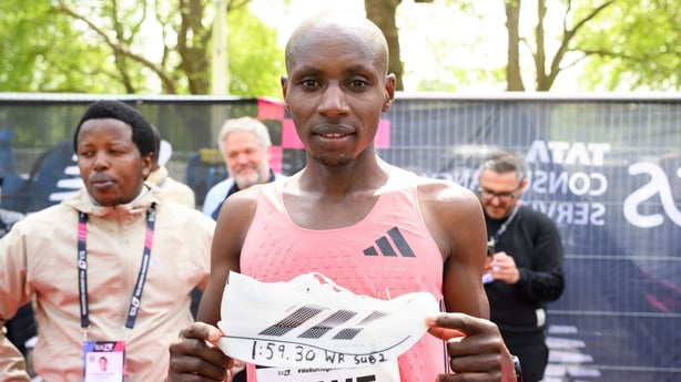 A runner in a pink vest holds his Adidas trainers 