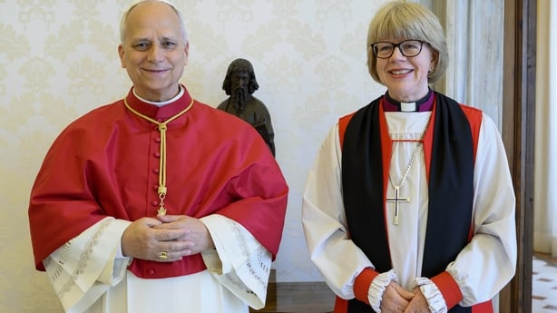 Image shows Pope Leo wearing red and white robes and Archbishop Sarah Mullally wearing white, black and red robes, standing next to each other, smiling.