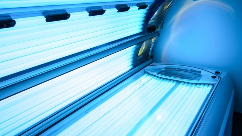 Image shows an open tanning bed illuminated with blue light