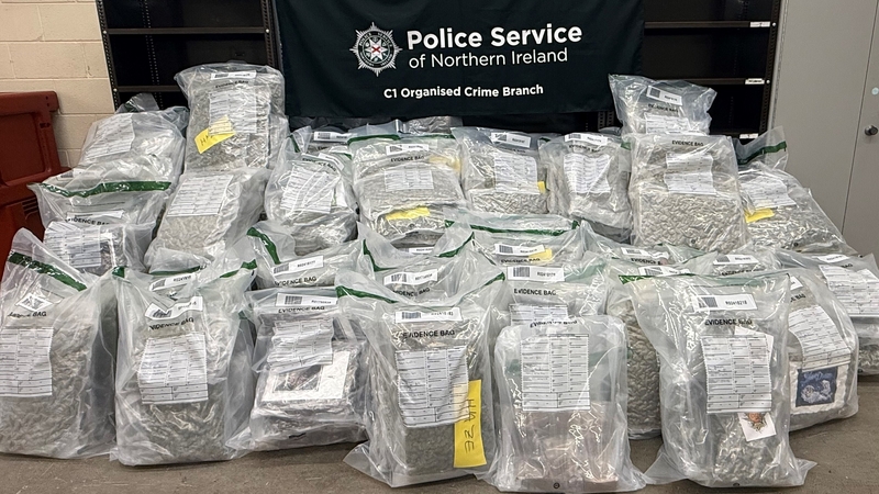 plastic bags of cannabis stacked on a table with a PSNI sign behind