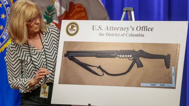A Justice Department staffer places a large photograph of a shotgun on display before a press conference at the Department of Justice