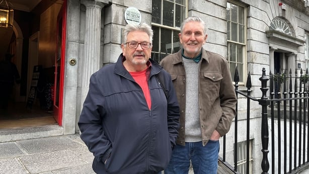 Dominic Taylor and Ron Carey stand side by side smiling at the camera. They are standing in front of a Georgian building in Limerick City