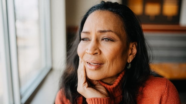 A woman in a red sweater gazes thoughtfully out of a window