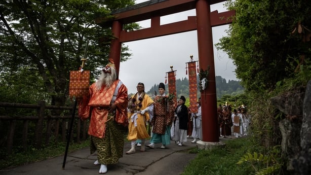 Devotees walk under a Torri gate, marking the entrance to a Shinto shrine, as they prepare to carry a portable shrine, holding a deity