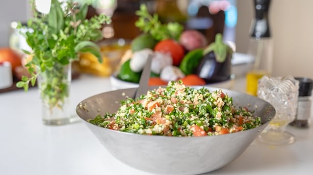 Close-up of a vibrant bulgur wheat salad with fresh herbs, tomatoes, and vegetables on a kitchen counter, capturing healthy eating, plant-based nutrition, and a fresh, wholesome lifestyle.