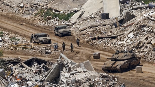 Israeli tanks and military vehicles standing along the road between destroyed houses in southern Lebanon near the border with Israel.