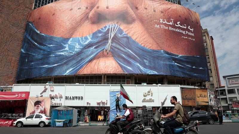 Motorists ride past an anti-US billboard referring to President Donald Trump and the Strait of Hormuz