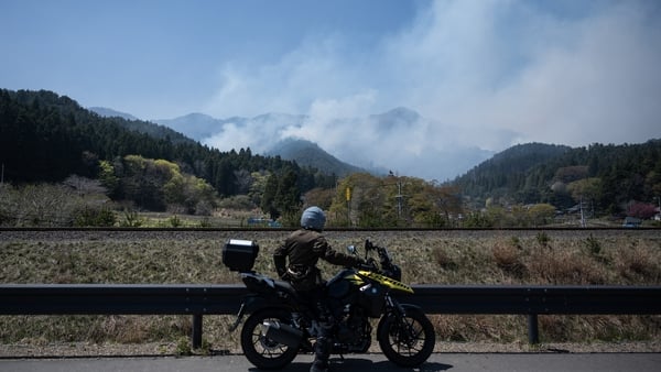 A man stops on his motorcycle to watch a fire burn in the hillsides in the town of Otsuchi in Iwate Prefecture