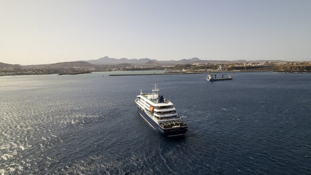 This aerial picture shows a general view of the cruise ship MV Hondius stationary off the port of Praia, the capital of Cape Verde, on May 3, 2026. An outbreak of "severe acute respiratory illness" on board a cruise ship in the Atlantic has left two people dead and a third in intensive care in Johan