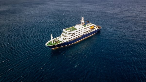 Aerial image shows a medium sized cruise ship sailing on the sea.