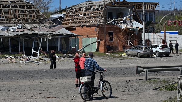 Residents walk past damaged buildings and cars at the site of a Russian missile strike in the town of Merefa, Kharkiv region