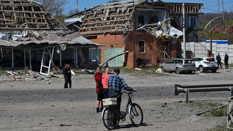 Residents walk past damaged buildings and cars at the site of a Russian missile strike in the town of Merefa, Kharkiv region