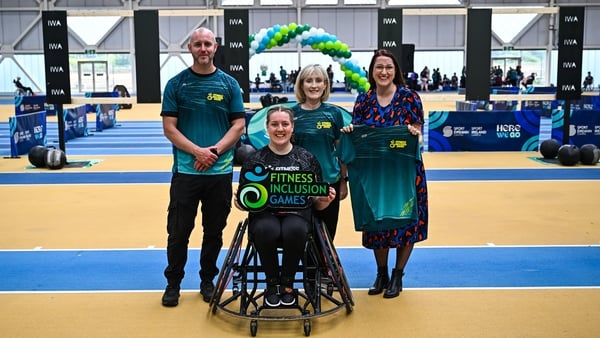 Three people stand alongside a fourth person in a wheelchair in a sports setting