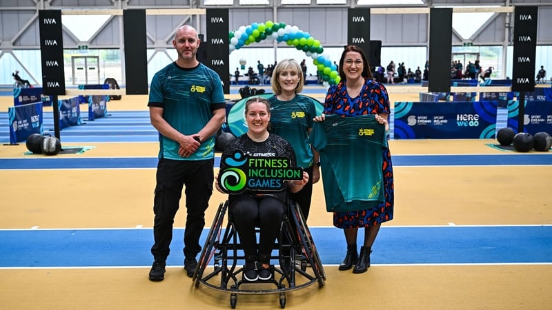 Three people stand alongside a fourth person in a wheelchair in a sports setting