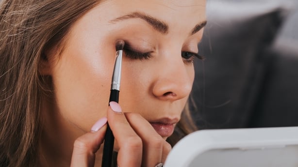 Close up portrait of beautiful young woman applying eyeshadow powder with brush.