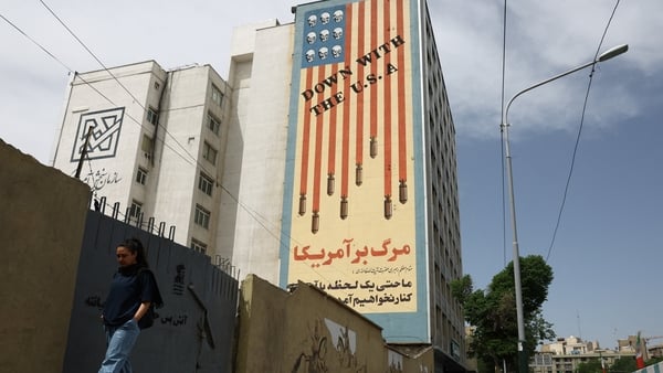 A woman walks past an anti-US mural on a building in Tehran