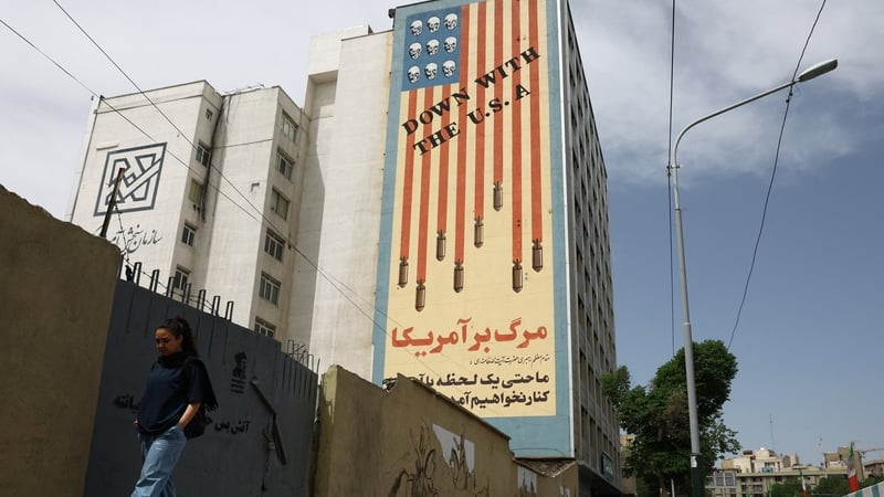 A woman walks past an anti-US mural on a building in Tehran