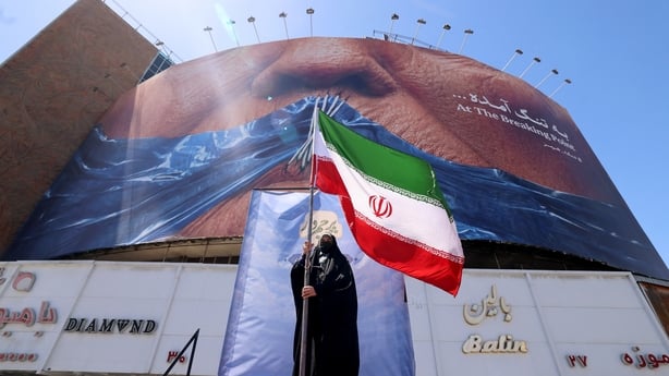 A woman holds the Iranian flag as she stands infront of an anti-US billboard 