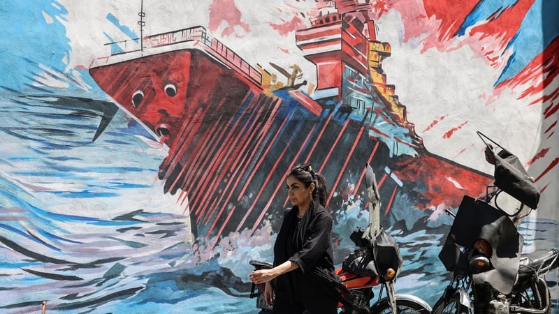 A woman walks past an anti-US and anti-Israel mural painted on a wal in Tehran