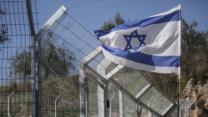 Israeli flags are seen flying beside a wire fence