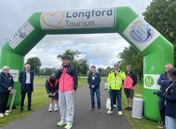 A young man stands beneath a temporary arch with the words 'Longford Tourism' on it