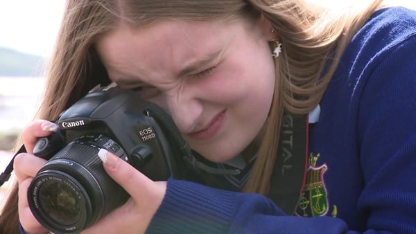 A young girl in school uniform takes a photo with a dslr camera.