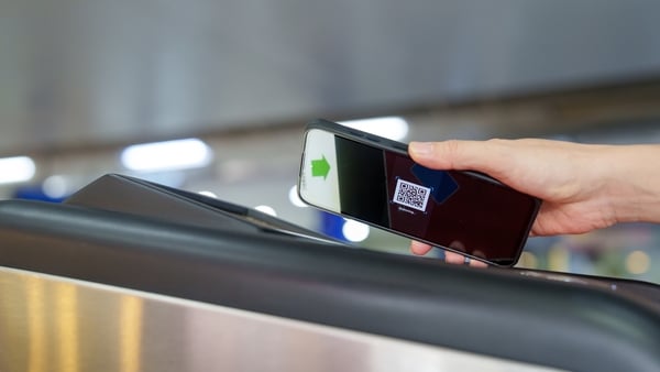 A person holding a mobile phone over a digital scanner at a public transport barrier