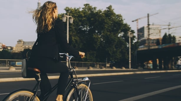 Image shows a woman with shoulder length blonde hair cycling in a city.
