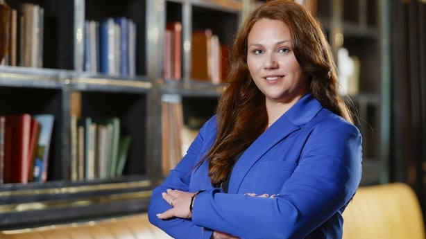 Photo of HRLocker CEO Crystel Robbis Rynne with arms folded wearing a blue blazer, standing in front of a bookcase